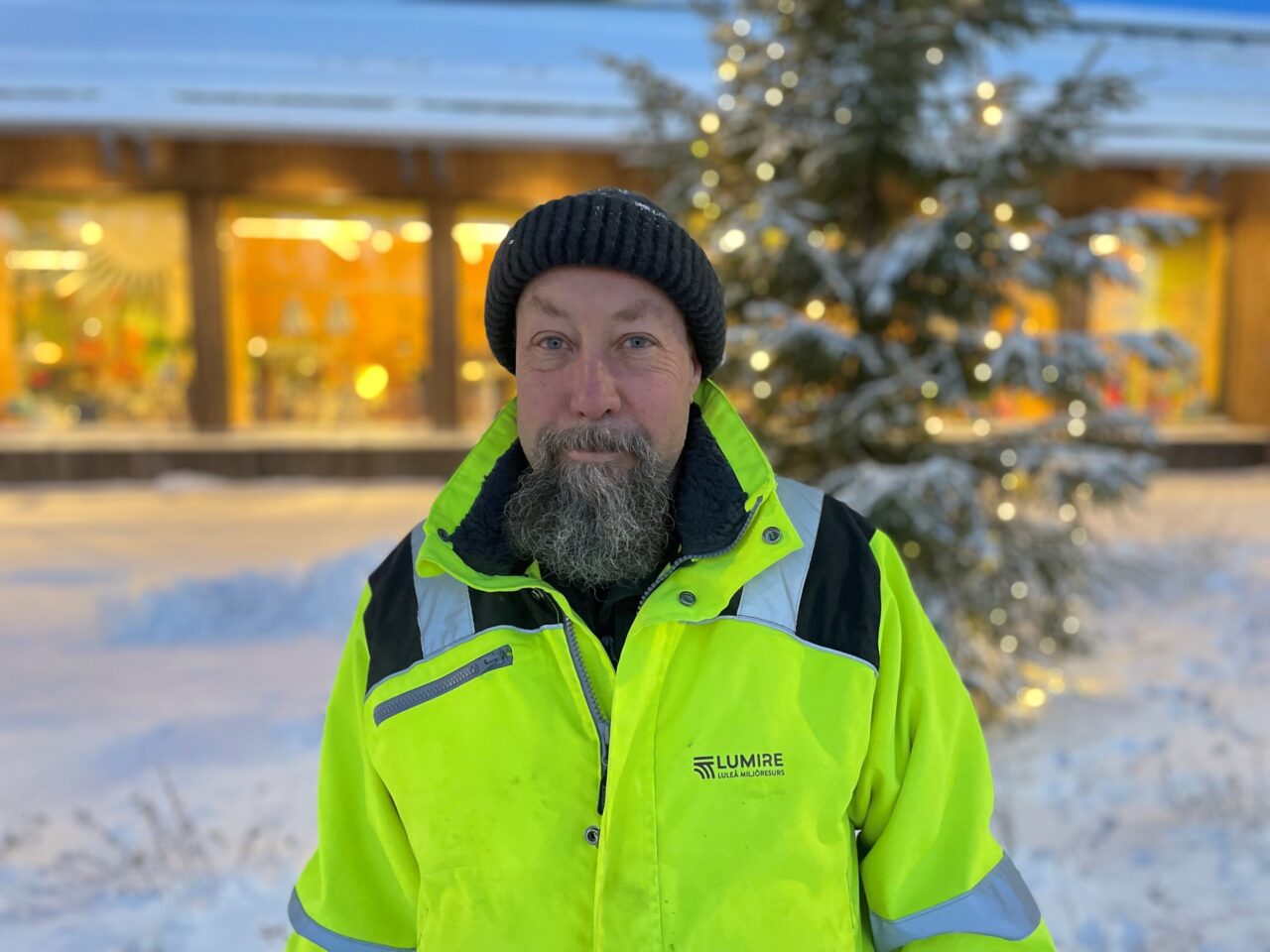 Bild på människa i gula varsel och arbetskläder i vintrigt landskap med julgran i bakgrund